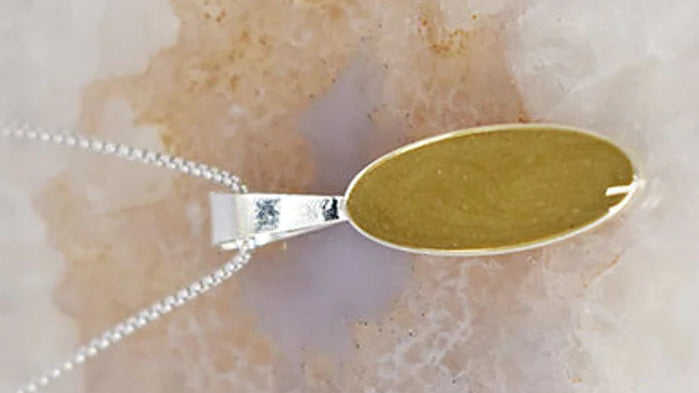 Close-up of Close By Me's Sterling Silver Long Oval Necklace set with ashes from aquamation, resting on a colorful geode surface.