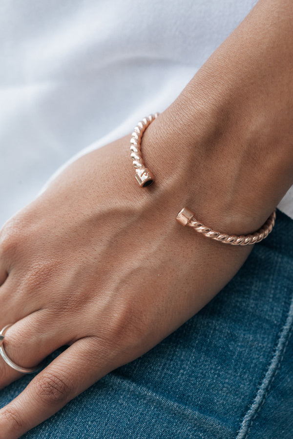 Rose gold cable cuff ashes bracelet on the arm of a model wearing a white t-shirt and blue jeans