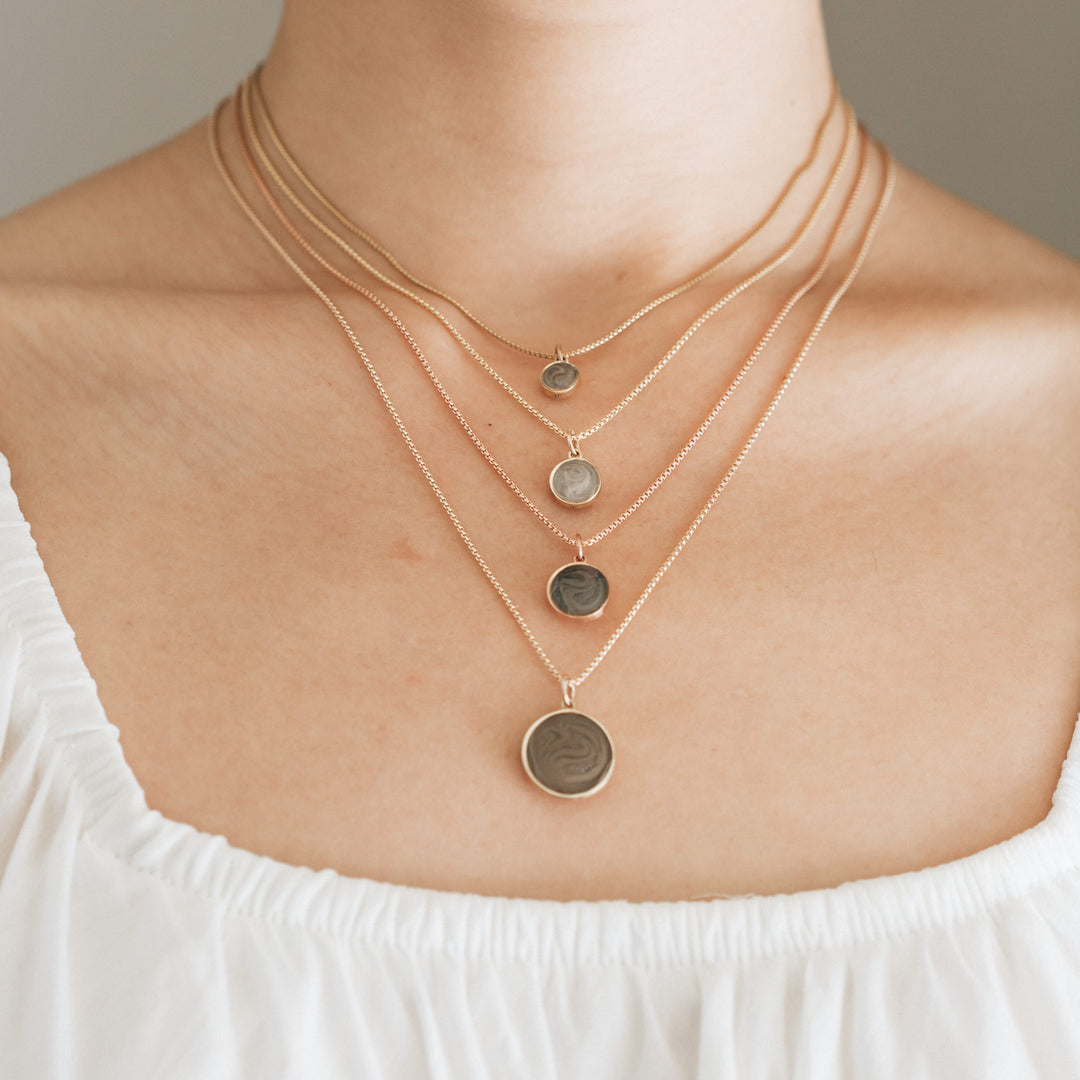 Close-up of a female model wearing Close By Me's 6mm, 8mm, 10mm, and 15mm Dome Cremation Pendants in 14k gold. Each pendant is worn on a different length chain so that they are layered from smallest to largest.