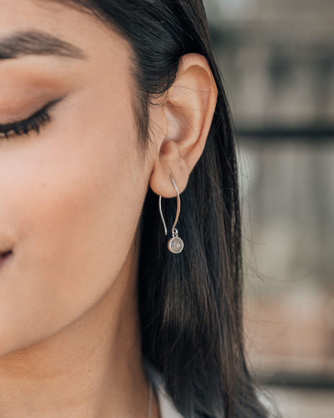 A model wearing a silver dangle earring with ashes