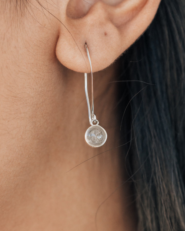 A very close up image of a woman wearing a dangle earring made with ashes by close by me jewelry
