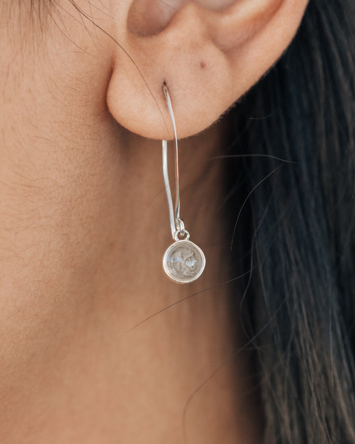 A very close up image of a woman wearing a dangle earring made with ashes by close by me jewelry