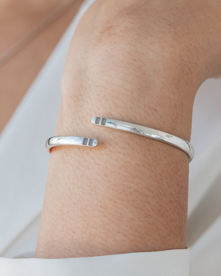 A very close up photo of a woman's wrist in a white blouse showing off the sterling silver bypass hinged cuff bracelet by close by me