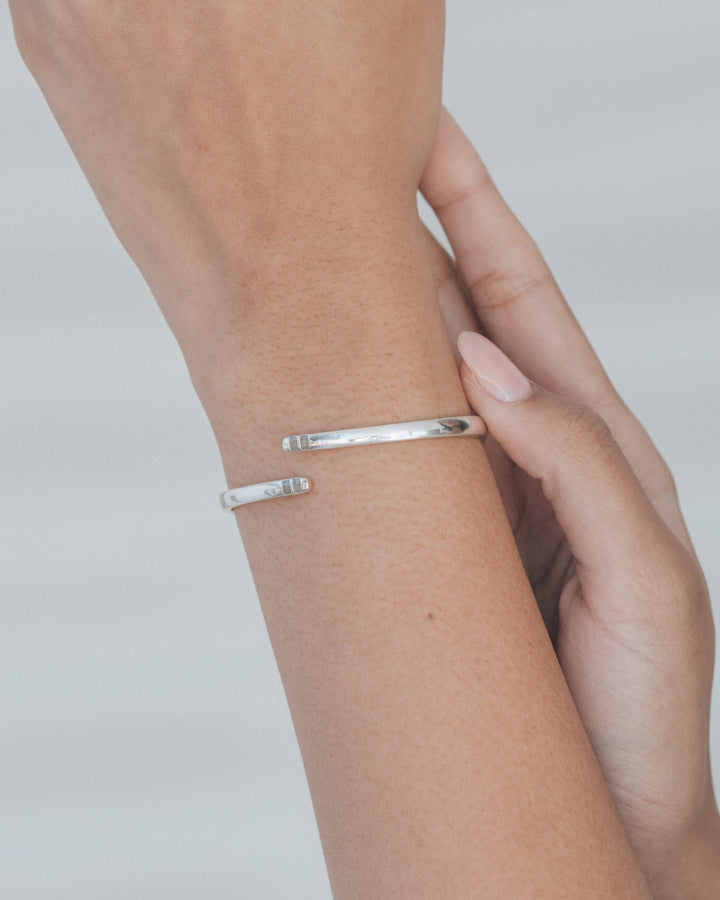 An artistic photo of a woman's extended arm showing off a hinged bypass cuff bracelet with ashes