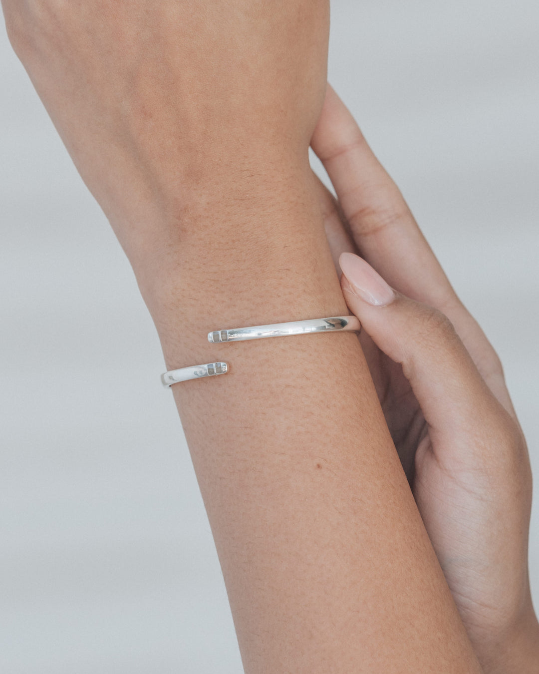 A photo of a woman holding up her wrist, on which she wears a memorial cuff hinged bypass style bracelet with ashes