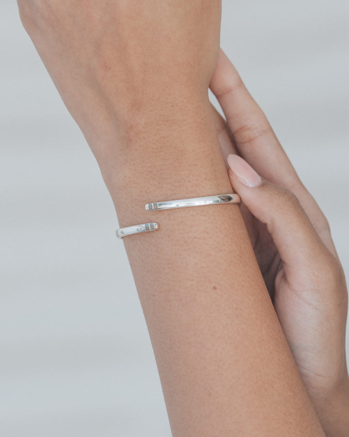A photo of a woman holding up her wrist against a white background to show the sterling silver bypass hinged cuff bracelet