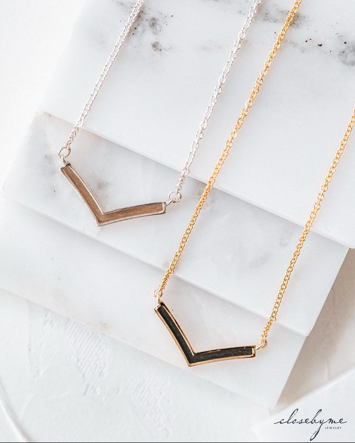 Both the sterling silver and 14k yellow gold versions of close by me jewelry's chevron memorial necklace lying flat against white marble