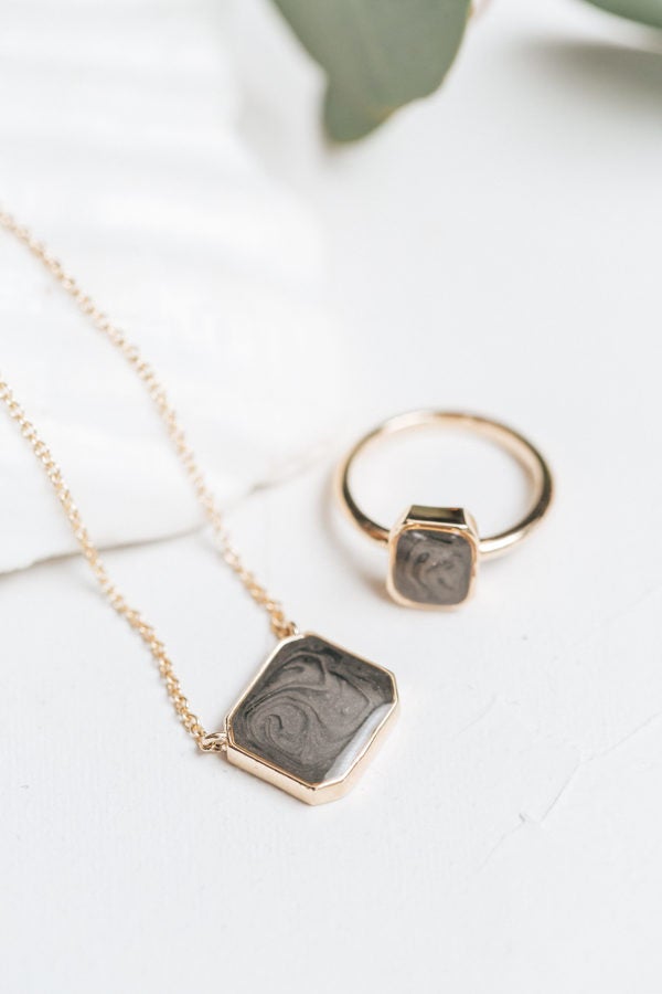 The cushion art deco cremains collection by close by me jewelry in 14k yellow gold lying flat against a white background