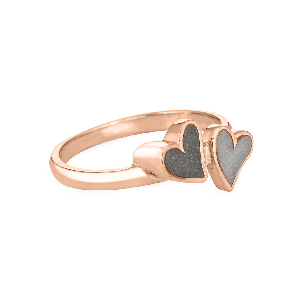 Side view of Close By Me's 14K Rose Gold Double Heart Cremation Ring, floating against a white backdrop. The left heart has a darker ashes setting, and the right heart has a light grey ashes setting.