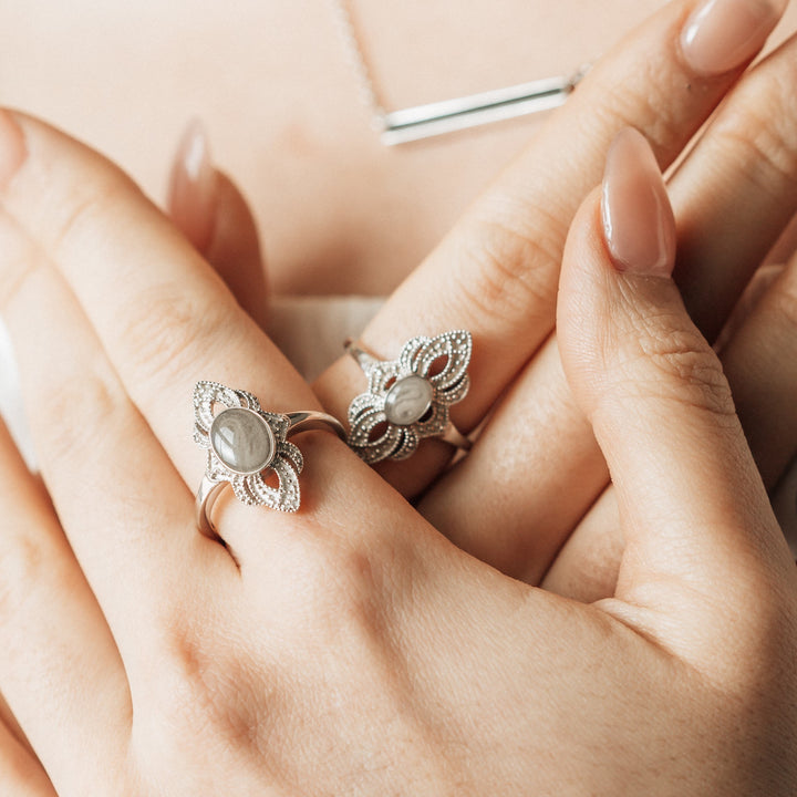 A close-up of a female model's hands crossed against her chest. On her left index finger is Close By Me's Large Setting World War II Cremation Ring; on her right is Close By Me's Small Setting World War II Cremation Ring.