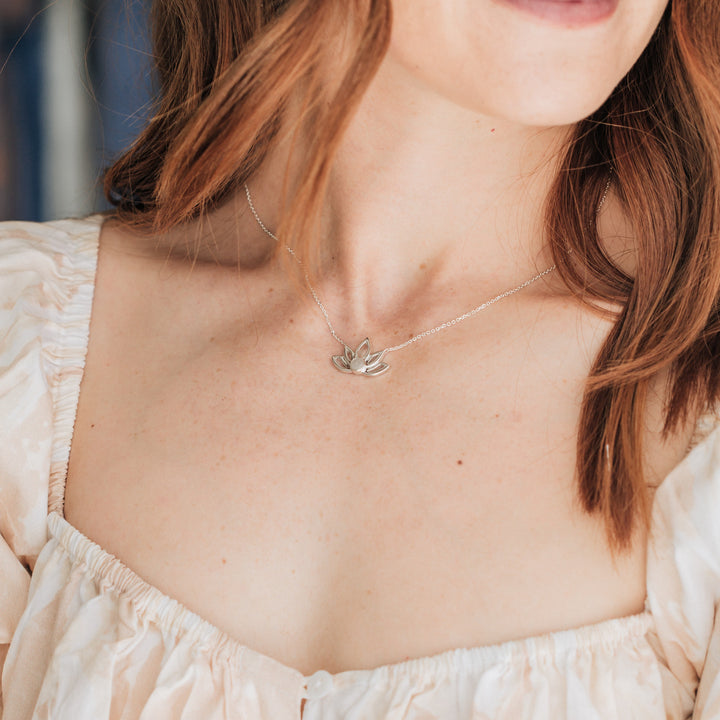 Pictured here is a model in a light peach dress with red hair wearing close by me jewelry's Sterling Silver Lotus Flower Necklace with ashes design