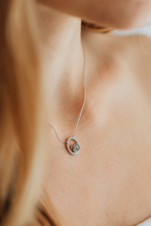 A close-up photo, taken off to the side, of Close By Me's Open Diamond Halo Cremation Necklace in 14K White Gold worn around the neck of a light-skinned, female model.