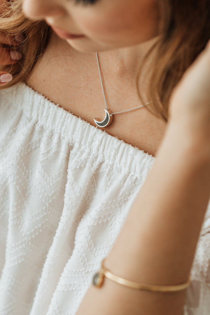 Overhead view of Close By Me's Crescent Moon Cremation Necklace being worn by a model.