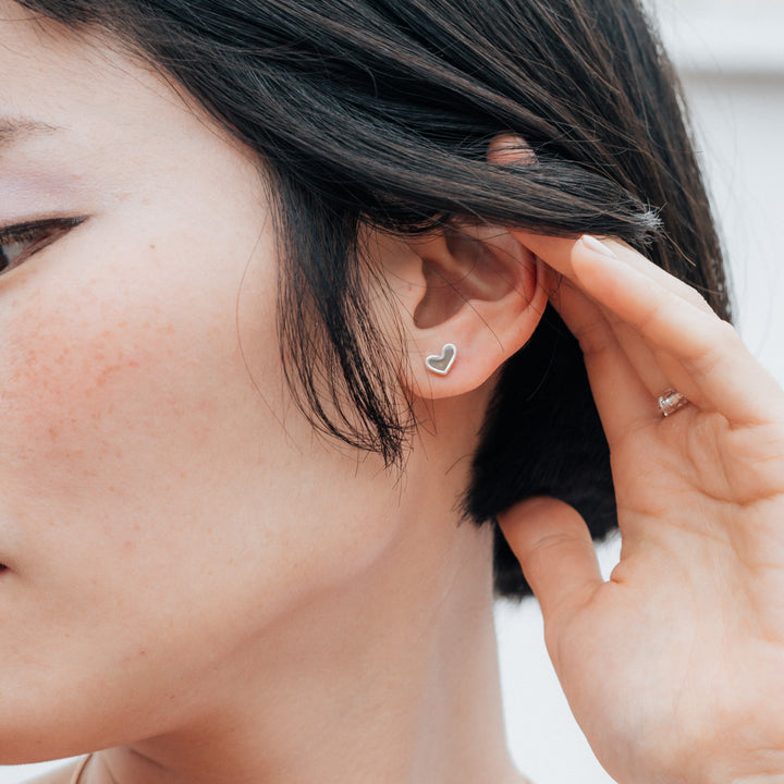 Signature heart stud cremation earrings in sterling silver shown on a model with short black hair close up