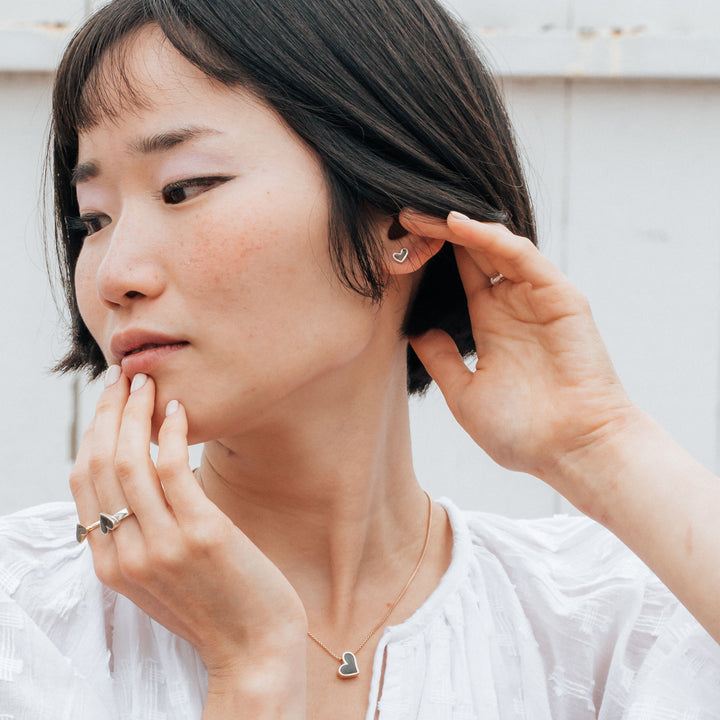 Signature heart stud cremation earrings in sterling silver shown on a model with short black hair