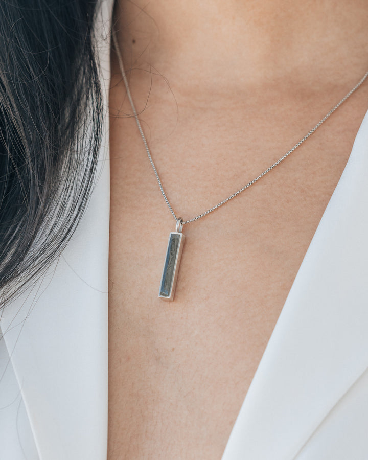 A model in a white blouse wearing a small bar cremains necklace designed to hold ashes in a pendant by close by me jewelry