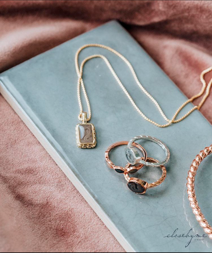 close by me jewelry's Cable Collection of memorial ashes pieces, all in different metals and lying on a bright blue ceramic plaque