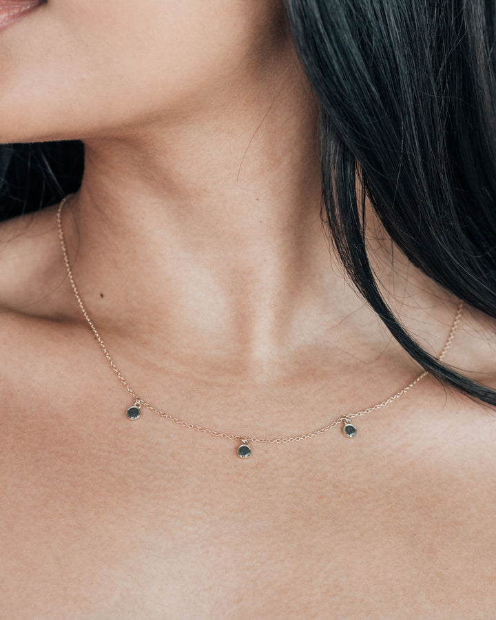 A close up showing a model wearing a dainty cremation necklace with three drop style components in sterling silver