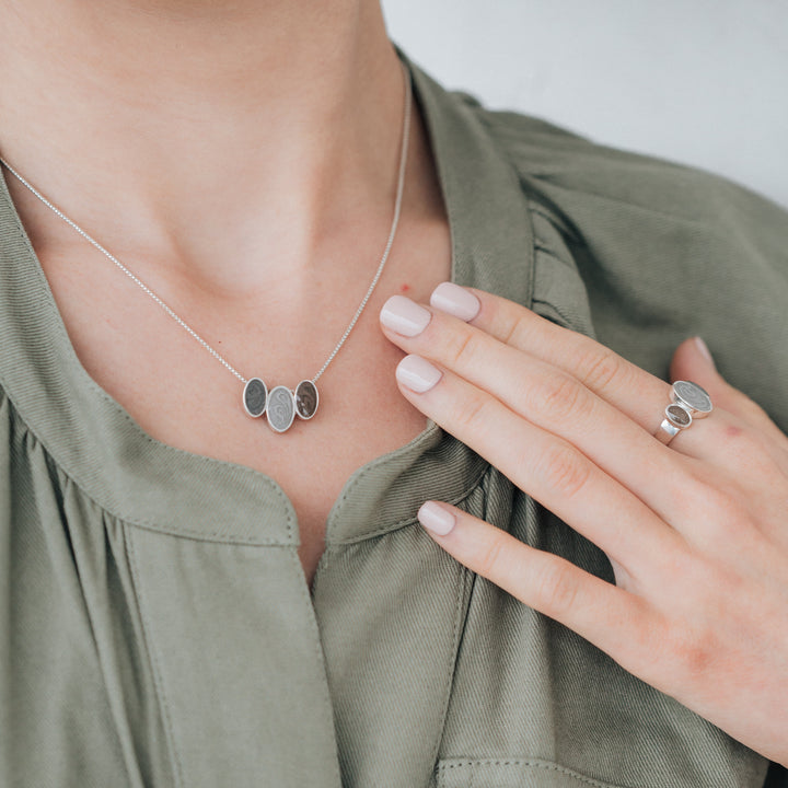A model in a green top wearing both the Sterling Silver Triple Oval Setting Ashes Ring and Pendant by close by me jewelry