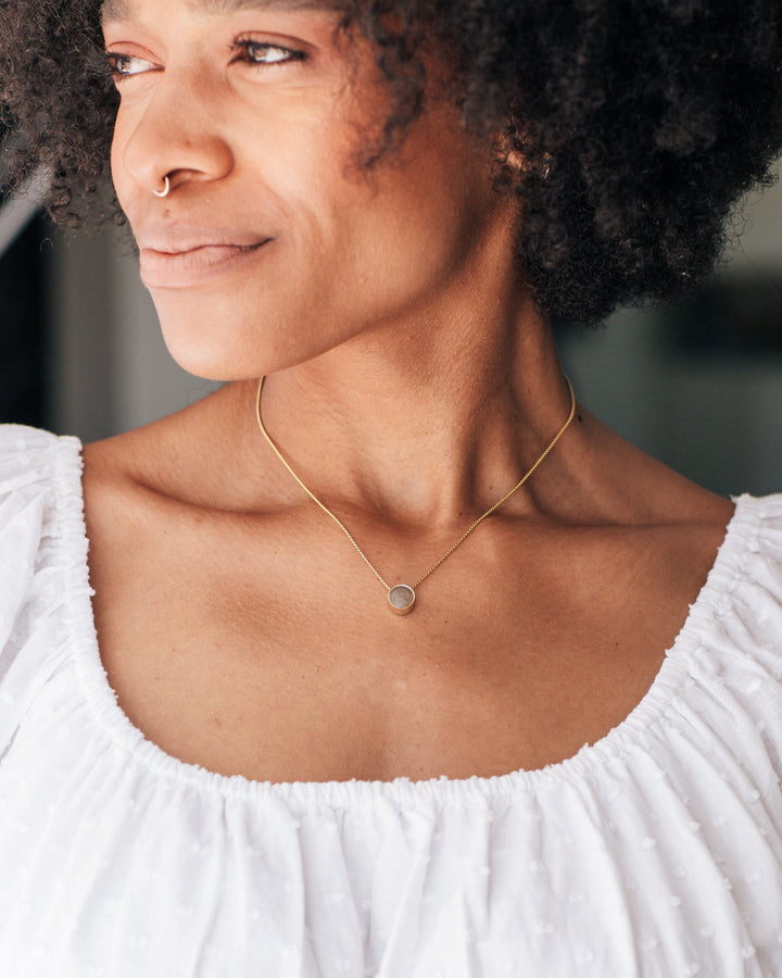 Pictured here is a model in a white blouse wearing close by me jewelry's 8mm Sliding Ashes Solitaire Necklace in 14K Yellow Gold