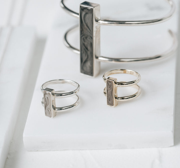 This stylized photo shows Sterling Silver ashes jewelry from close by me jewelry's Bar Collection sitting upright on a flat white stone