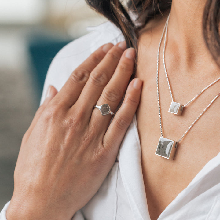 This photo shows a model wearing the Hexagon White Baguette Diamond Band Ring by close by me jewelry in 14K White Gold on the middle finger of her hand as she rests it against her chest