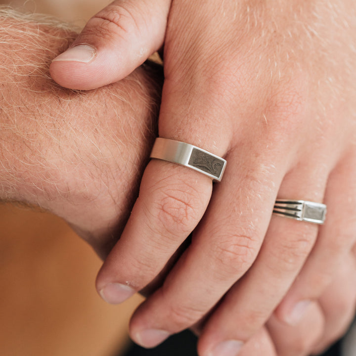 This photo shows a male model wearing several pieces of Sterling Silver Men's Cremation Jewelry. The Men's Classic Band Ashes Ring design is on his index finger.