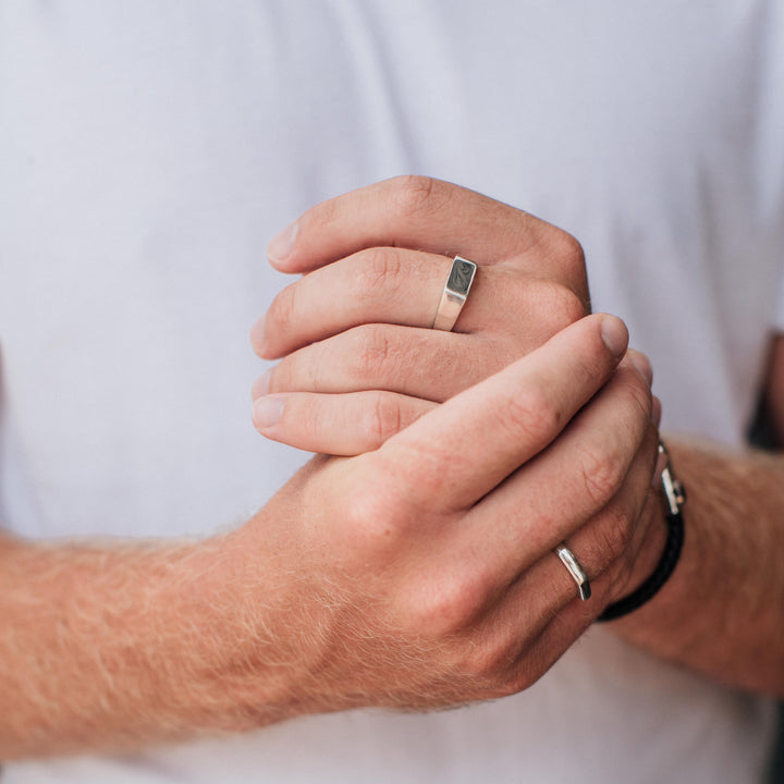 This photo shows a male model wearing close by me jewelry's Men's Rectangle Signet and Smooth Band Rings in Sterling Silver