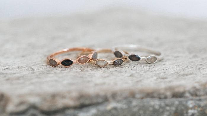 Close By Me Jewelry's Four Setting Cremation Ring in 14K Rose Gold, Two Setting Cremation Ring in 14K Yellow Gold, and Three Setting Ring in Sterling Silver resting on a stone surface.