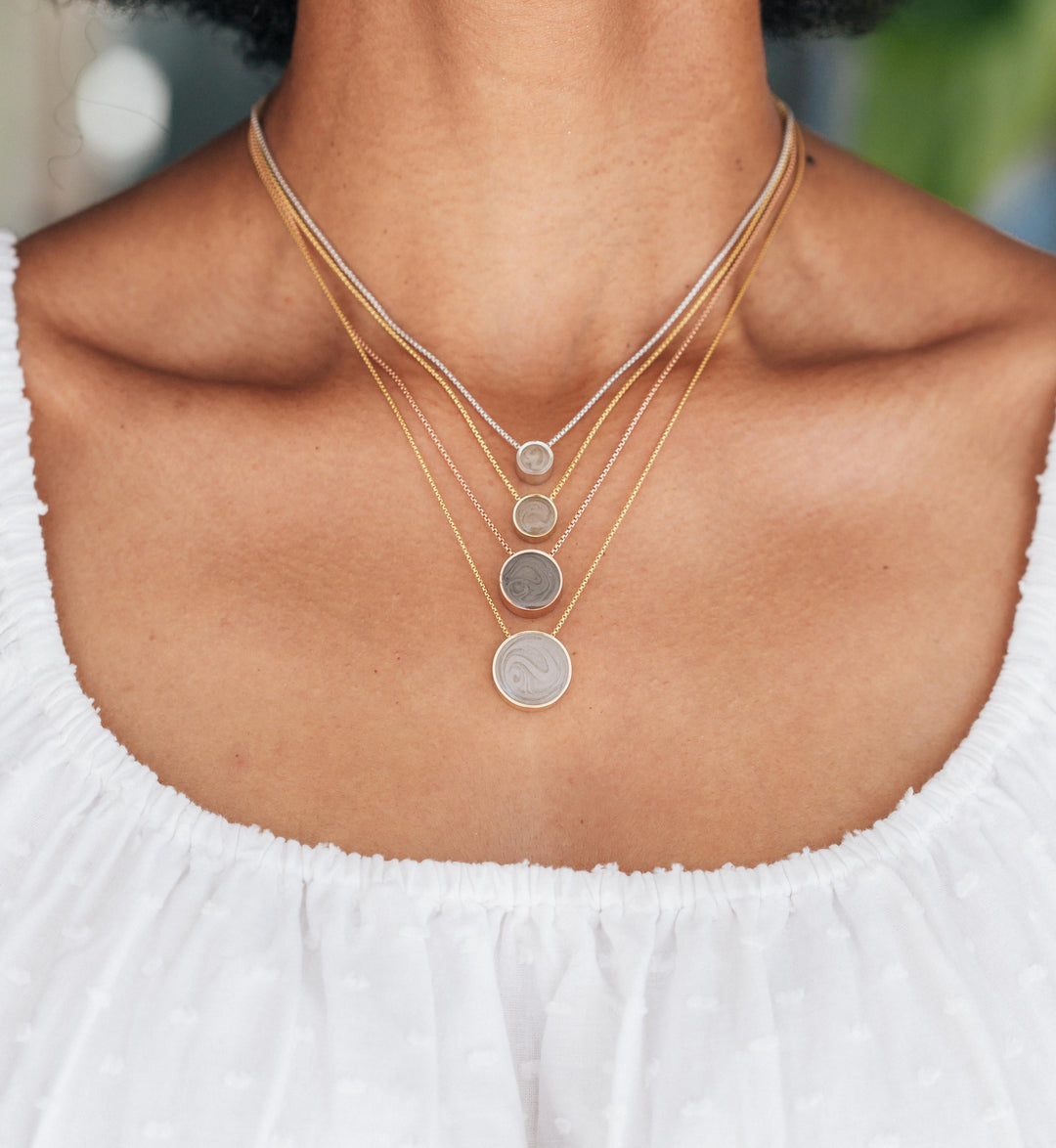 Close By Me's 6mm, 8mm, 12mm, and 15mm Sliding Solitaire Cremation Necklaces on a model. Each pendant is on a different length chain to create a layered effect that goes from smallest at the top to largest at the bottom.