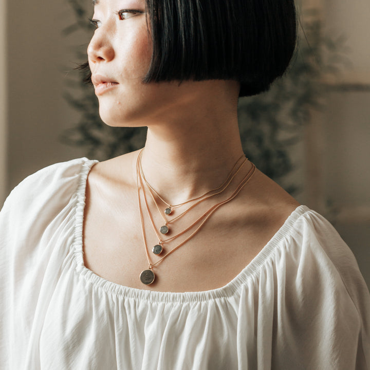 This photo shows a model with dark hair in a white top wearing all sizes of close by me jewelry's Dome Cremation Pendant series in 14K Rose and Yellow Gold
