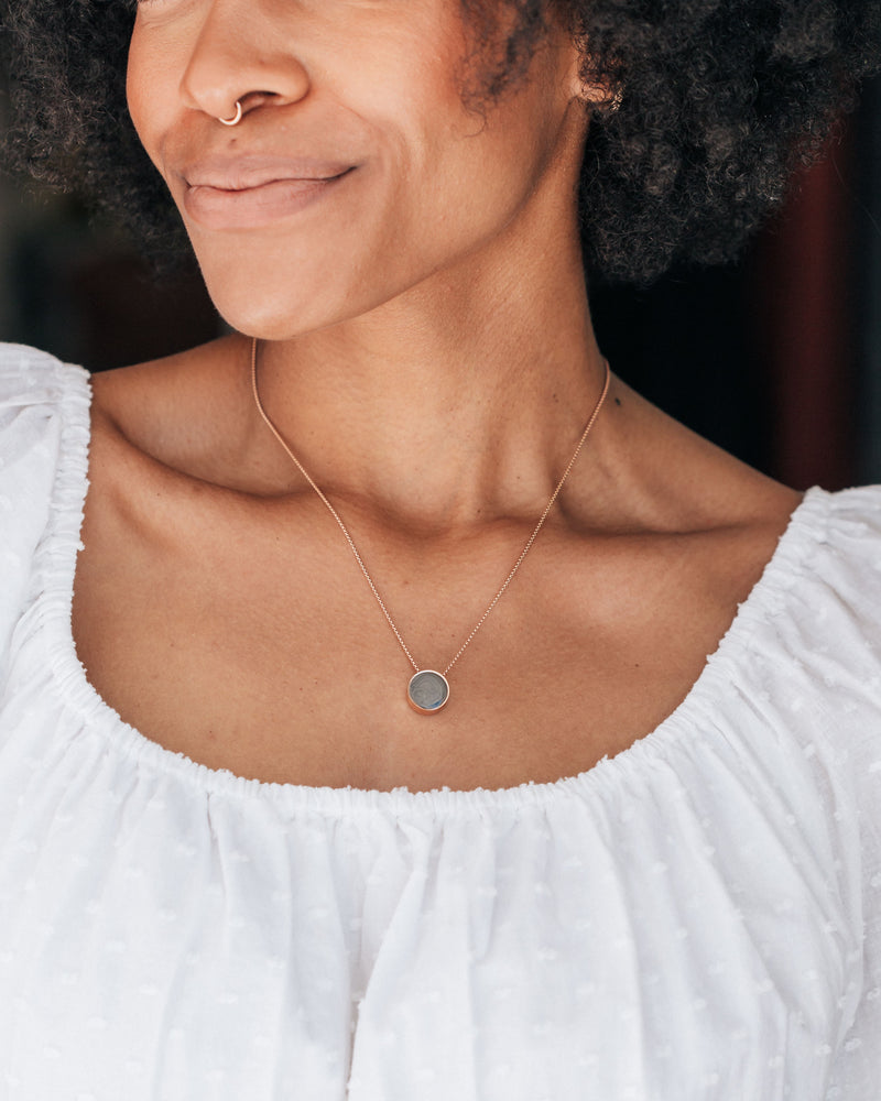 This photo shows a dark skinned model in a white top wearing the Sliding Solitaire Ashes Necklace by close by me jewelry in a 12mm size in Sterling Silver