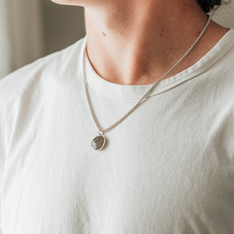 A male model in a white t-shirt wearing the sterling silver dome ashes necklace with a thick chain by close by me jewelry
