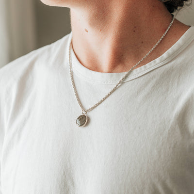 A male model in a white t-shirt wearing the sterling silver dome ashes necklace with a thick chain by close by me jewelry