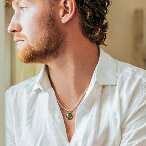 A male model in a white button down looking to the side while he wears a 15mm dome ashes pendant on a thick chain