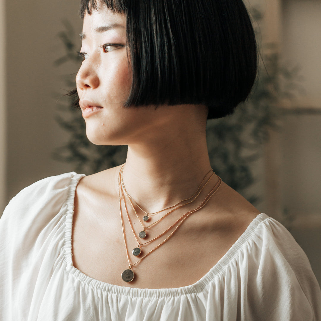 A model in a white top wearing all sizes of close by me jewelry's dome memorial pendant series in various metals