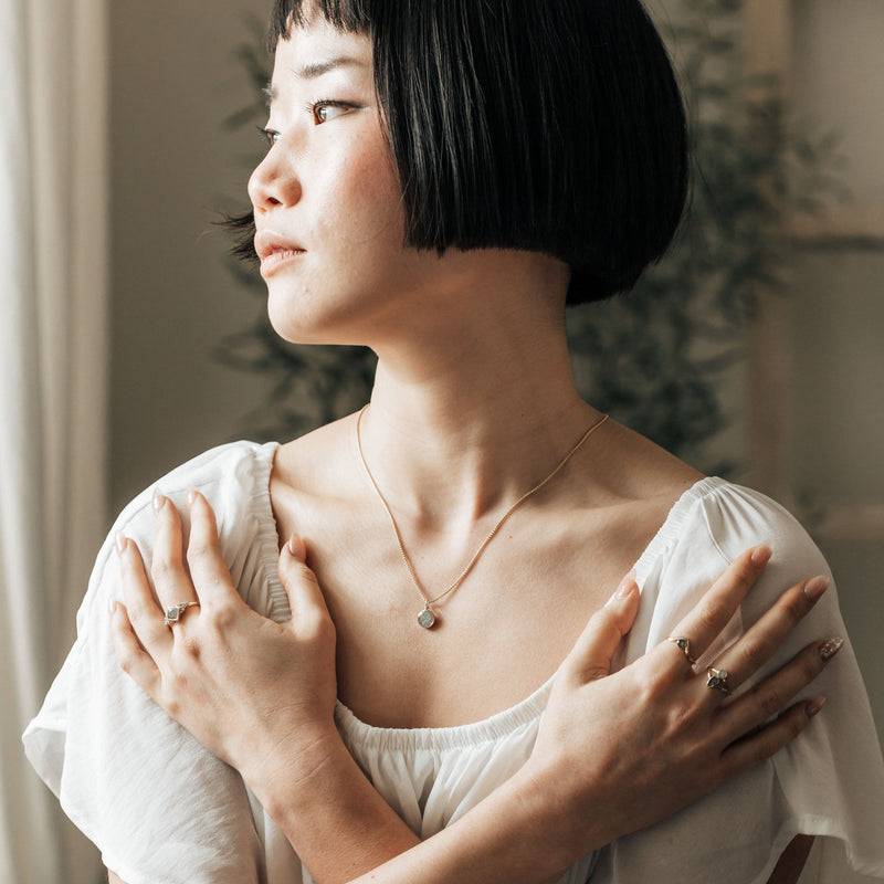 A model in a white top wearing the 14k yellow gold 8mm dome necklace with ashes by close by me jewelry along with many other ashes pieces