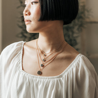 A model in a white top wearing all sizes of close by me jewelry's dome memorial pendant series in various metals