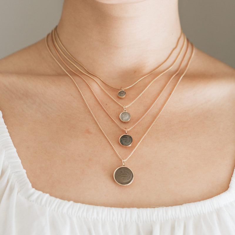 A close up showing all sizes of dome ashes necklaces by close by me jewelry on a model