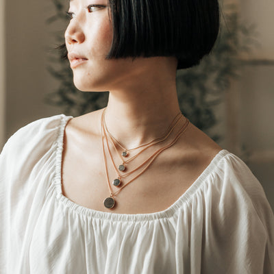 A model in a white top wearing all sizes of close by me jewelry's dome memorial pendant series in various metals