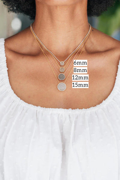 This photo shows all of the sizes of Sliding Solitaire Ashes Pendant designed by close by me jewelry around a model's neck and labeled with each size