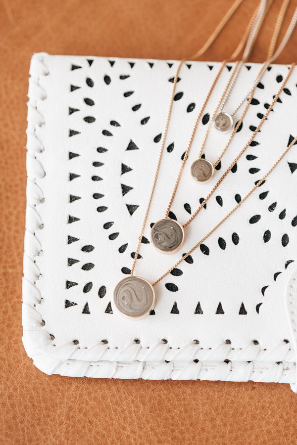 This photo shows all sizes of close by me jewelry's Sliding Solitaire Ashes Necklaces laid out flat on white fabric with cutouts over a light brown surface