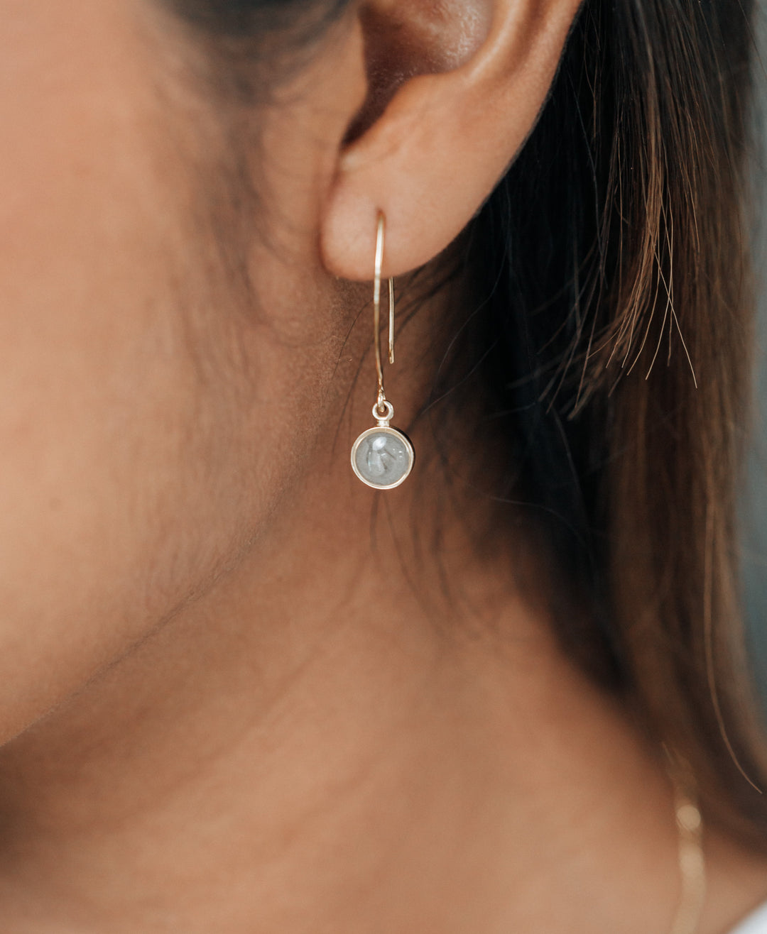 a close up showing a silver ashes earring with a dome setting and arched ear wire in a model's ear