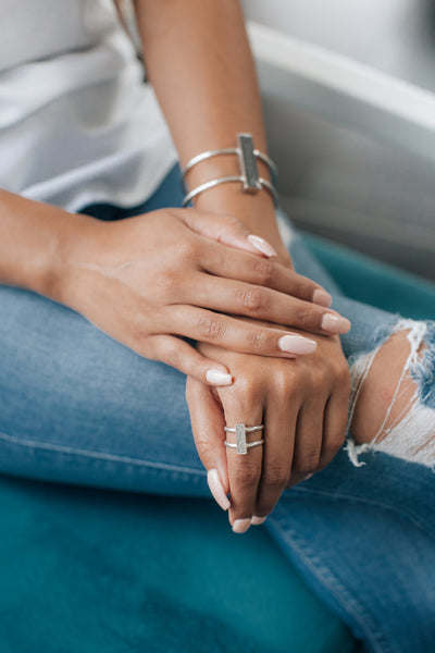 Bar Cremation Bracelet in Sterling Silver shown on the arm of a model, this also shows the Bar Ring in Sterling Silver, pictured on the finger of the opposite hand as both hands rest on her thigh.