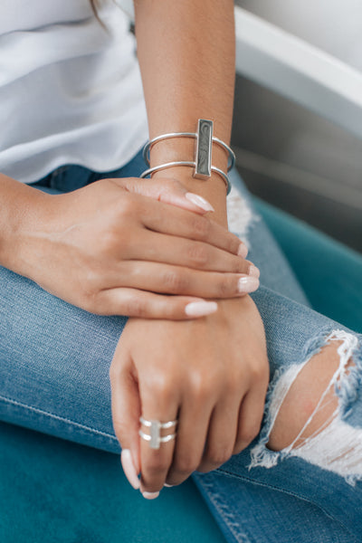 Bar Cremation Bracelet in Sterling Silver shown on the arm of a model, this also shows the Bar Ring in Sterling Silver, pictured on the finger of the opposite hand, the ring is out of focus while the bracelet is in focus.