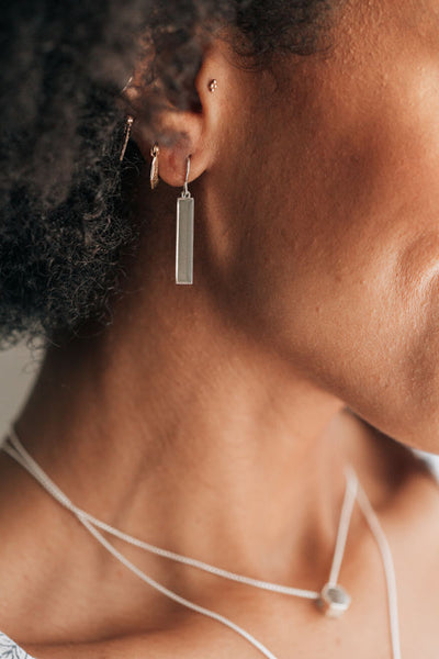 a close up showing a sterling silver bar dangle earring design with ashes hanging from a model's ear