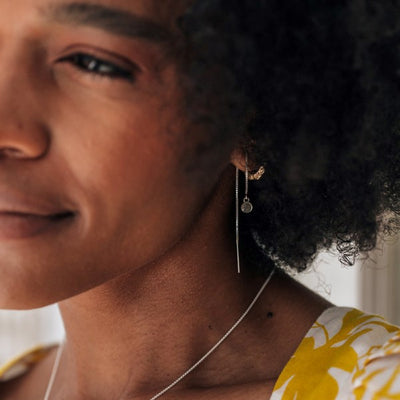 This photo shows close by me jewelry's Bilateral Cremains Chain Earrings in Sterling Silver being worn by a dark-skinned model in a yellow and white dress