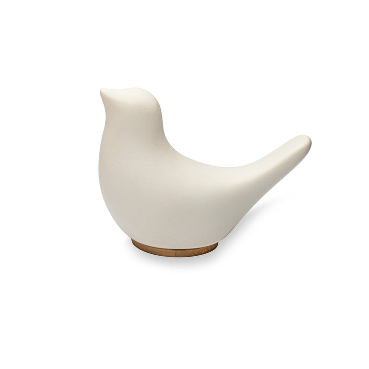 A side view of Close By Me's Ceramic Bird Urn facing to the left, against a solid white background. The urn has a matte white finish and its bamboo lid is visible at the bottom, doubling as a small pedestal.