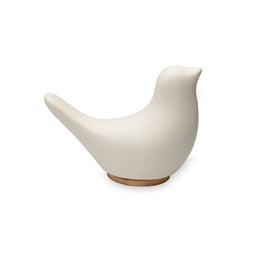 A side view of Close By Me's Ceramic Bird Urn facing to the right, against a solid white background. The urn has a matte white finish and its bamboo lid is visible at the bottom, doubling as a small pedestal.