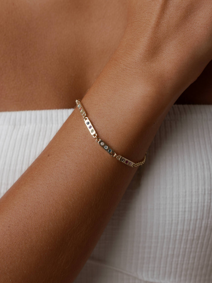 The Tribute Bracelet by Close By Me in 14K Yellow Gold on a model's wrist. It has five links with three different birthstones in each.